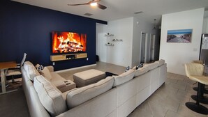 Ein modernes Wohnzimmer mit großem Flachbildfernseher, Deckenventilator, einer Couch und einem Essbereich.