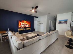 A modern living room with a large flat-screen TV, a ceiling fan, a sofa, and a dining area. - Family Friendly House Near Disney And Universal (Haines City)