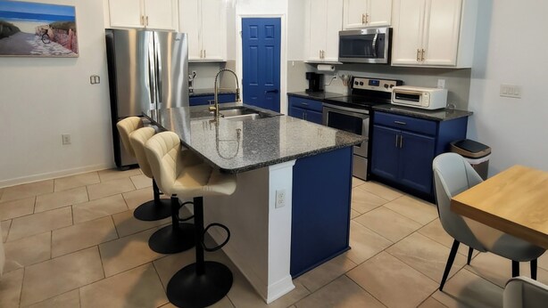 Eine moderne Küche mit weißen und blauen Schränken, Edelstahlgeräten, einer blauen Tür sowie einem Essbereich mit Holztisch und Barhocker.