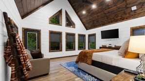 Una stanza con un letto, una TV, un soffitto in legno e ampie finestre.