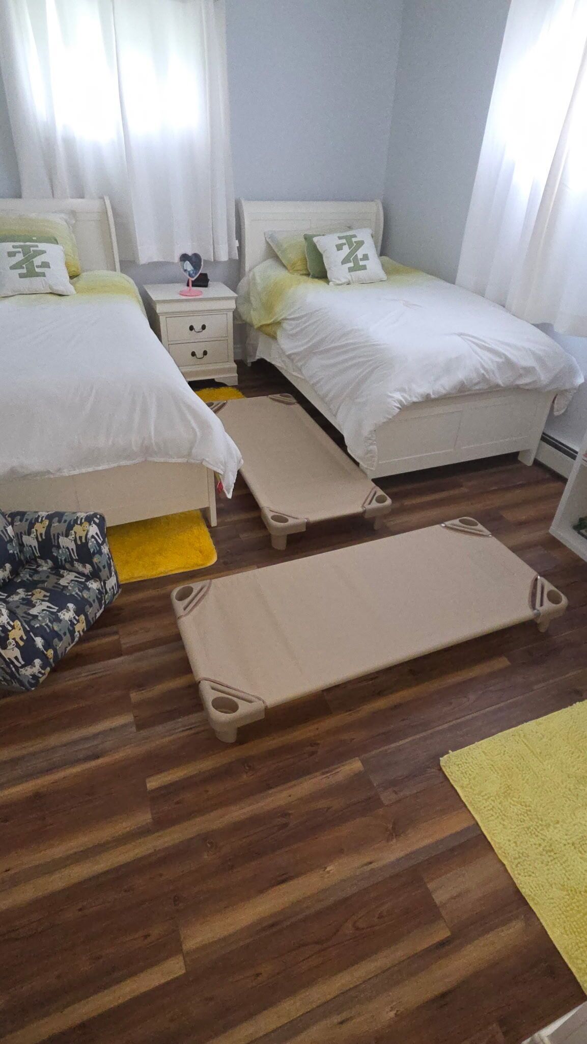 A bedroom with two beds, a nightstand, a bedside table, a small chair, and a portable cot.