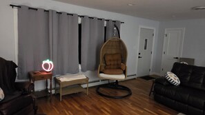 Una habitación con una silla colgante, una mesita de noche con lámpara, un sofá y una puerta.