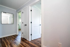 Um corredor com piso de madeira, paredes brancas e uma porta com puxador preto.