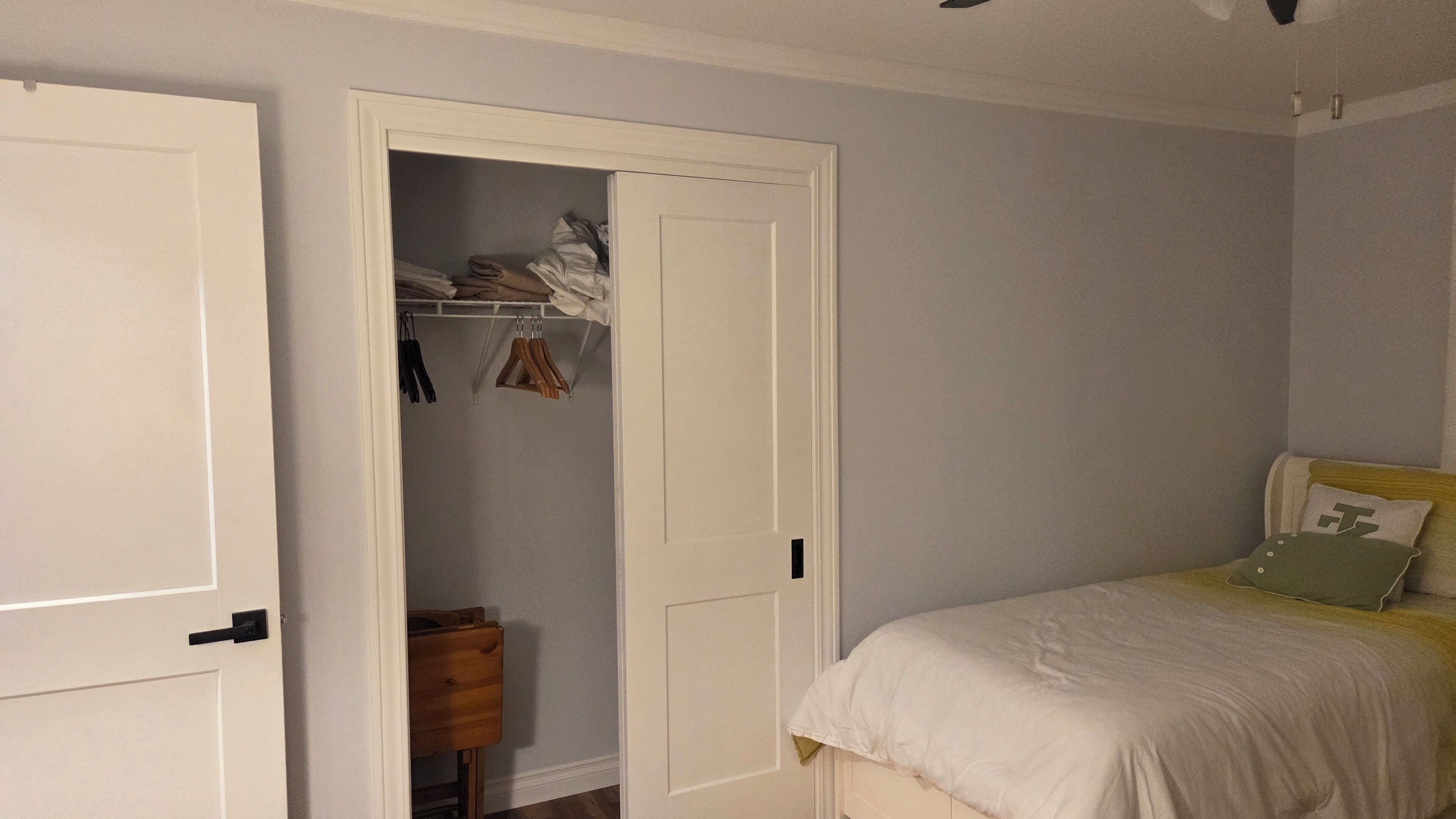 A bedroom with a bed, a closet with hanging clothes, and a wooden nightstand.