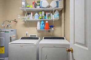 A laundry room with two front-loading washers, a shelf with cleaning supplies, and a water heater.