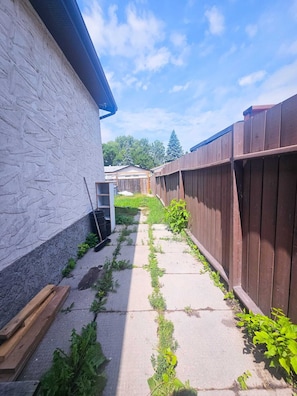 A narrow concrete pathway flanked by a white textured wall and a wooden fence. - Winnipeg South Goust house (Winnipeg)