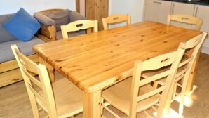 Un'area pranzo con tavolo e sedie in legno, una poltrona con cuscini e un angolo cottura con pensili e lavello.