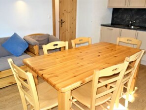 Ein Essbereich mit Holztisch und Stühlen, einer Couch mit Kissen sowie eine Küchenzeile mit Schränken und Spüle.