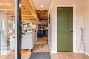 A modern interior with a wooden ceiling, a kitchen with a black and white patterned backsplash, and a green door.