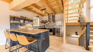 Una cucina moderna con travi in legno, un'isola centrale, sgabelli da bar e una scala.