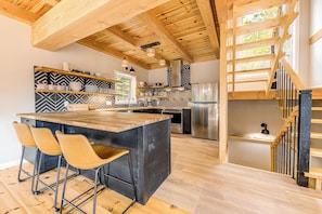 Una cocina moderna con vigas de madera, una isla central, taburetes de bar y una escalera.