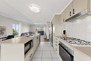 A modern kitchen with a central island, a stove, and a refrigerator. - Modern 2BR Mango Hill Stay | Close to Shops & Rail (City of Moreton Bay)