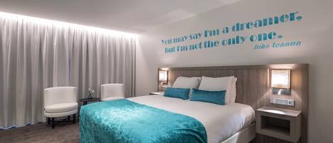 Habitación de hotel con una cama grande, dos mesitas de noche, un cabecero y una cita en la pared.