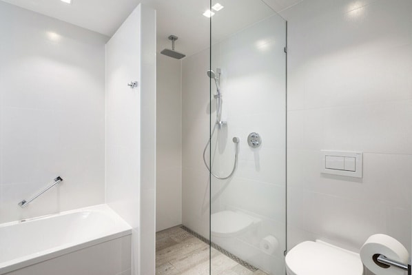 Ein modernes Badezimmer mit einer gläsernen Duschkabine, einer weißen Badewanne und einem WC.