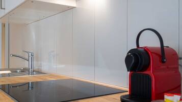 Cocina moderna con un lavamanos de acero inoxidable, una cocina de inducción negra y una tetera roja sobre la encimera.