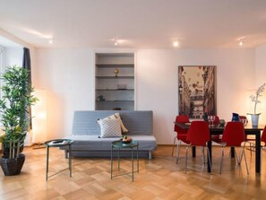 A modern living room with a grey sofa, a dining table with red chairs, a small side table, and a potted plant. - LU Neptun I - Chapel bridge HITrental Apartment by Interhome (Lucerne)