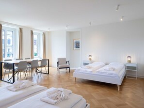 A hotel room with a large bed, a dining table with chairs, a chair, a bedside table with a lamp, and a window with curtains. - Apartment  by Interhome (Lucerne)