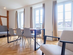 Una habitación moderna con una mesa de comedor, sillas, un sofá y ventanas amplias con vista a la ciudad.