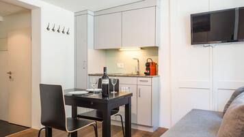Eine kompakte Küchenzeile mit Essbereich, einem flachbildfernseher an der Wand und einer Tür mit Kleiderhaken.