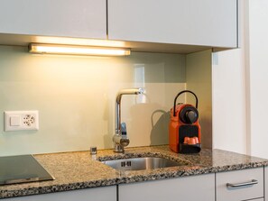 Ett kök med en diskho i rostfritt stål, en blandare, en bänkskiva och en kaffebryggare.