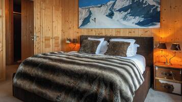 A wooden-paneled room with a bed, two bedside lamps, a wooden nightstand, and a painting of a snowy mountain landscape.