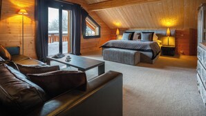 A cozy log cabin bedroom with a bed, a sofa, a small table, and a window with curtains.