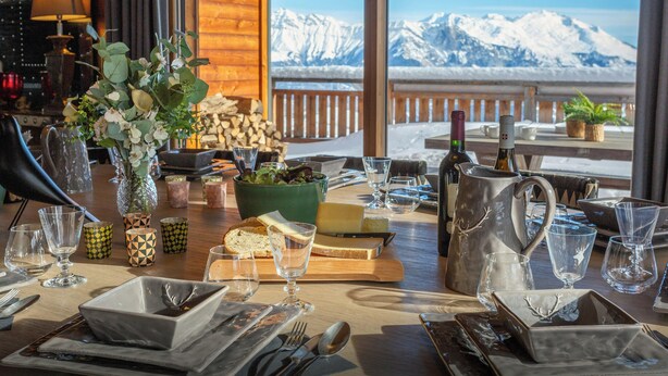 A dining table set with glassware, plates, and a bottle, overlooking a snowy mountain view.