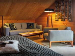 A cozy loft bedroom with a sloped ceiling, a grey sofa, a grey armchair, a wooden coffee table, and a floor lamp.