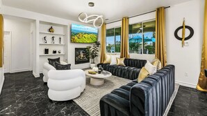 Una sala de estar moderna con chimenea, un conjunto de sofás, un sillón blanco y un televisor grande.