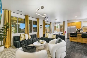 Un salon moderne comprenant un canapé, des fauteuils, une table basse et un coin cuisine avec un réfrigérateur.