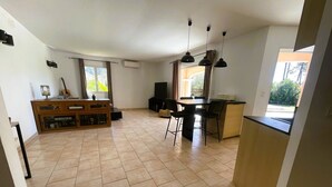 Een ruime woonkamer met een eettafel, stoelen, een houten kast en een gitaar.