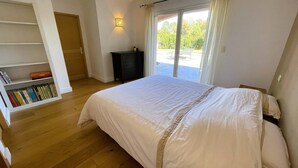 Een slaapkamer met een bed, een boekenkast, een dressoir en een schuifdeur naar buiten.