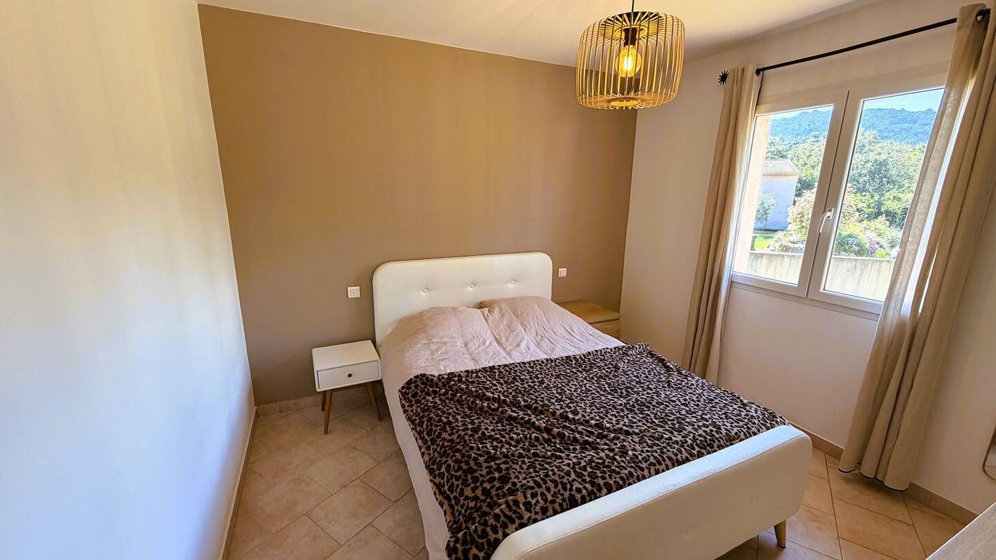 A bedroom with a bed, a nightstand, a window with curtains, and a hanging light fixture.