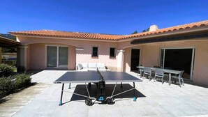 Een terras buiten met een tafeltennistafel, een zithoek met een bank en stoelen, en een gebouw met een pannendak.