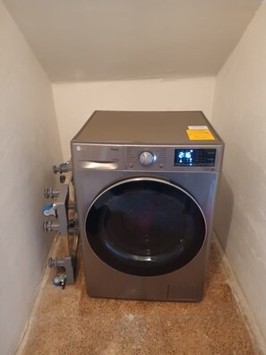 Eine kompakte, frontbeladene Waschmaschine aus Edelstahl mit digitaler Anzeige, eingebaut in einem kleinen, gefliesten Raum mit einer Wand.