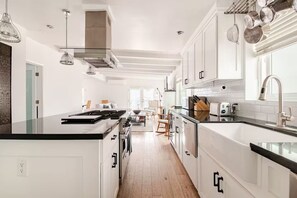 A modern kitchen with white cabinetry, a black countertop, stainless steel appliances, and pendant lighting.