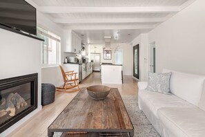 A modern living room with a fireplace, a wooden coffee table, a white sofa, and a kitchen in the background.
