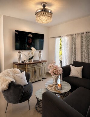 A modern living room with a flat-screen TV, a chandelier, a sofa set, a coffee table, and a cabinet. - Fast Wi-Fi, Great Location, and Comfort at SFM (San Francisco de Macorís)