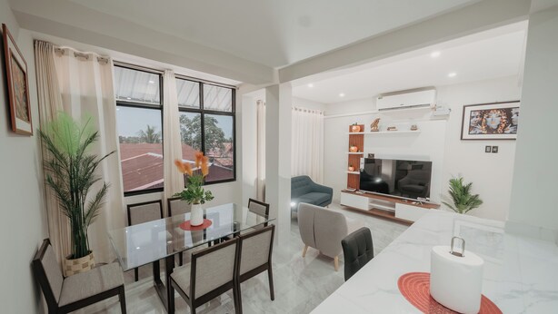 A modern living room with a TV, sofa, and dining area with chairs and a glass table. - KOA LIVING (Pucallpa)
