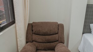 A brown reclining chair with a headrest and armrests in a room with a bed and a window. - KOA LIVING (Pucallpa)