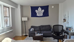 Een kamer met een bed, een bureau, een stoel, een bank, een Canadese vlag en een raam.