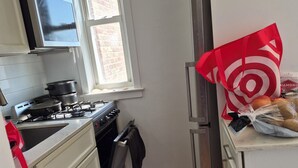 Een kleine keuken met witte kastjes, een fornuis en een raam.