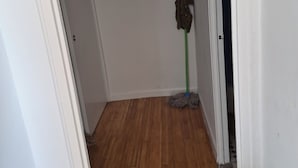 Een gang met houten vloer, een dweil tegen de muur en een koffer op de vloer.