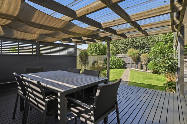 Eine Außenpatio mit Tisch und Stühlen, einem überdachten Pergola und Blick auf einen Garten.