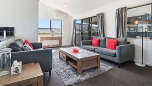 Ein modernes Wohnzimmer mit einem grauen Sofa, einem Holztisch und einem großen Fenster mit Vorhängen.