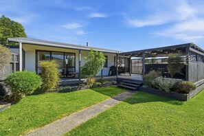 Ein modernes Haus mit überdachter Terrasse, einem Rasen und einem Kiesweg.