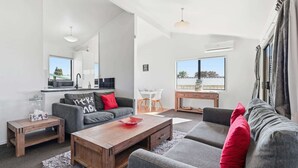 Ein modernes Wohnzimmer mit einem grauen Sofa, einem Holztisch und einem Essbereich mit einem weißen Tisch und Stühlen.