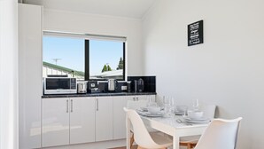 Eine moderne Küche mit weißen Schränken, einem Esstisch für vier Personen und Blick auf eine grüne Landschaft durch das Fenster.