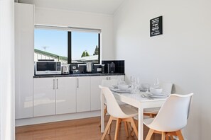 Une cuisine moderne avec des meubles blancs, une table à manger dressée pour quatre personnes et une vue sur un paysage verdoyant par la fenêtre.