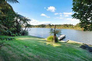 A lakeside view with a grassy area, a dock, and dense foliage. - Okere Tree House - Lakefront with own Jetty! (Okere Falls)